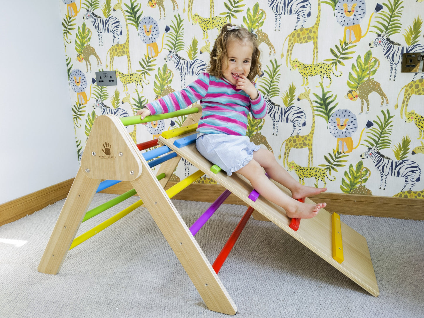 Little girl sitting on the ramp of a pikler climbing frame